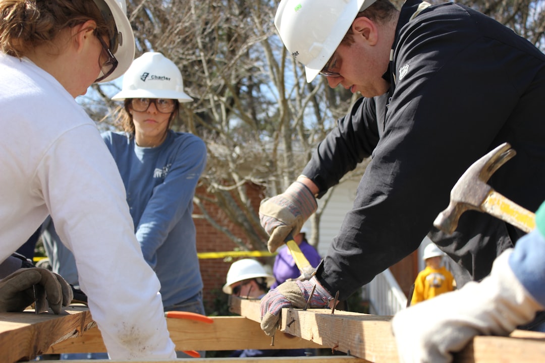 Volunteers working together to construct affordable housing, wearing hard hats and using construction tools