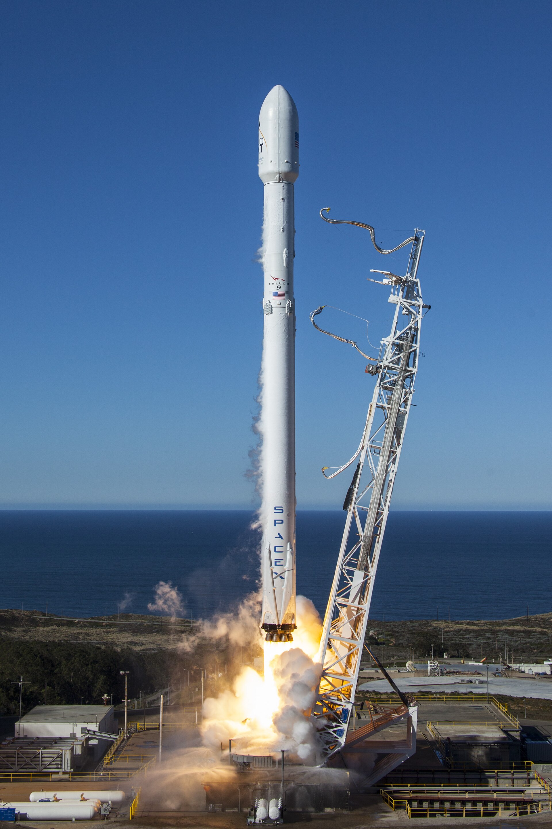A SpaceX Falcon rocket lifting off from the launch pad against a clear sky