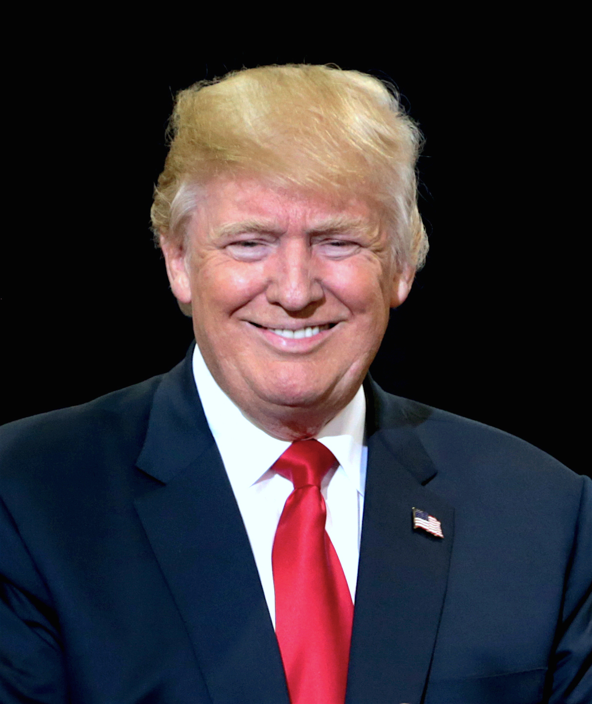 Donald Trump speaking at a political campaign rally with supporters and American flags behind him